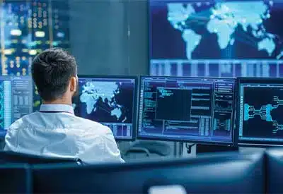 Analyst monitoring cybersecurity data on multiple screens